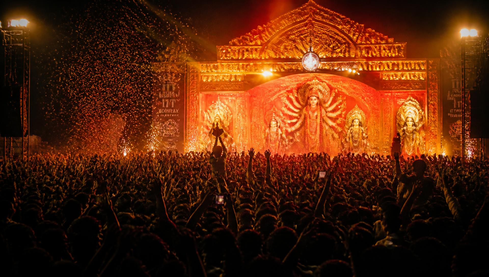 A crowd of thousands at a Durga Puja-inspired festival stage lit in vermilion and gold